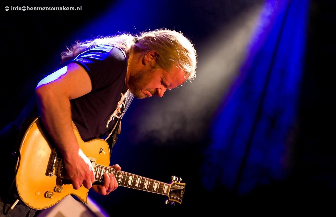 Joop Wolters on stage, playing a gold-top electric guitar under blue light